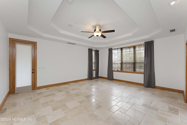 unfurnished room featuring a tray ceiling, baseboards, visible vents, and ceiling fan