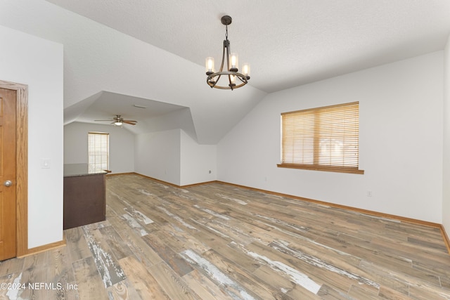 additional living space with baseboards, vaulted ceiling, light wood-style floors, a textured ceiling, and a notable chandelier