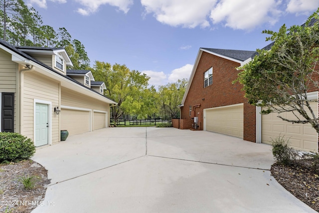 view of property exterior with brick siding, driveway, and fence