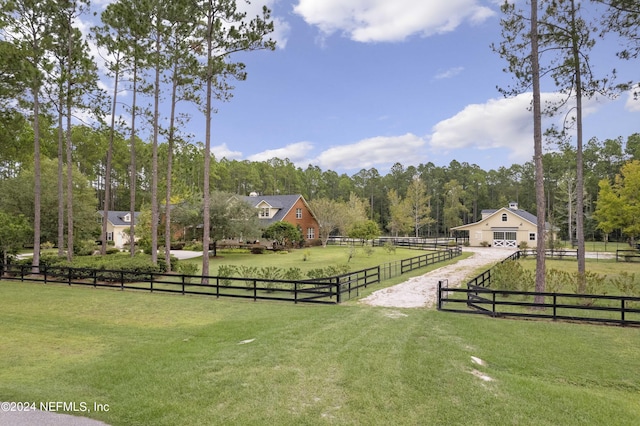 view of property's community featuring a rural view, a lawn, a garage, and fence