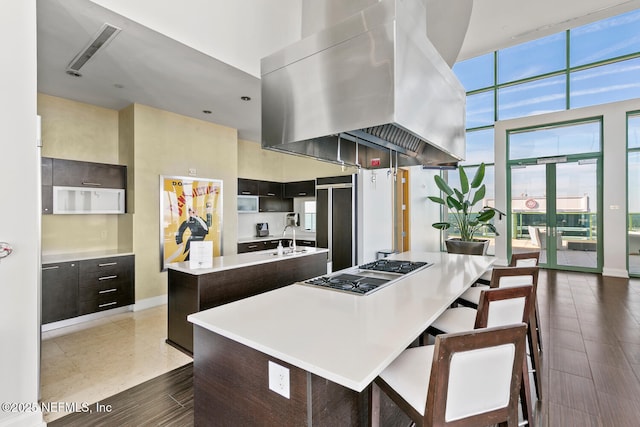 1431 Riverplace Blvd Unit 2606, Jacksonville, FL 32207 - kitchen featuring light countertops, island exhaust hood, stainless steel gas cooktop, a center island with sink, and a high ceiling