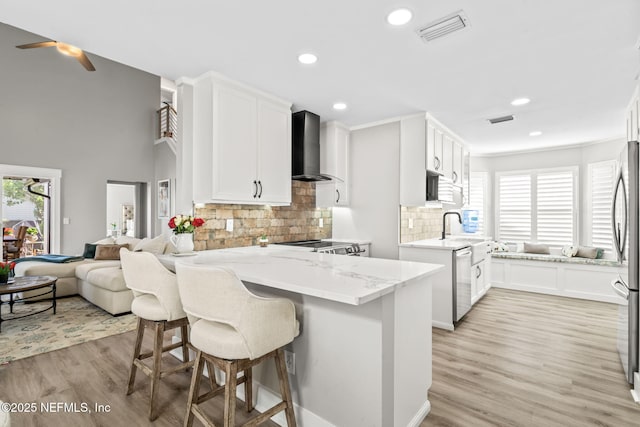 kitchen with light stone counters, visible vents, a peninsula, stainless steel appliances, and wall chimney exhaust hood