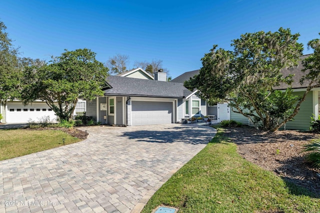 view of front of house with a front lawn, decorative driveway, an attached garage, a shingled roof, and a chimney