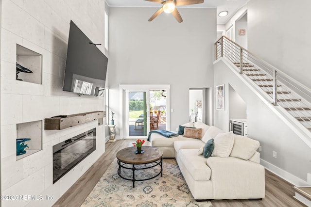 living area featuring baseboards, a tiled fireplace, stairs, a high ceiling, and wood finished floors