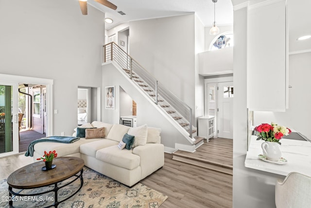 living room with visible vents, wood finished floors, baseboards, ceiling fan, and stairs