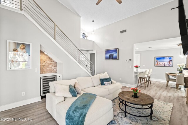 living room featuring visible vents, baseboards, stairway, wood finished floors, and high vaulted ceiling