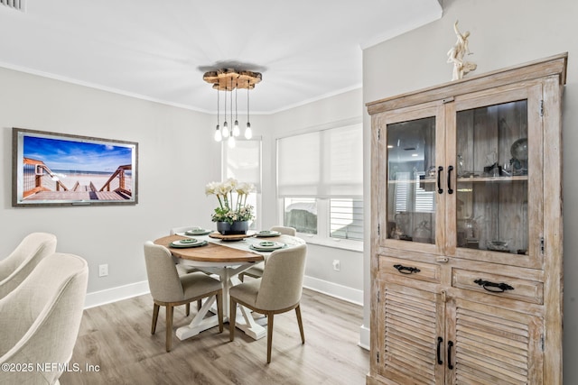 dining area with baseboards, crown molding, and light wood finished floors