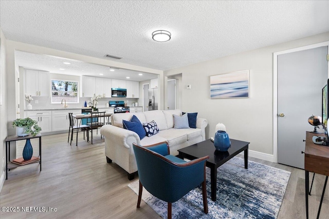 living area with baseboards, visible vents, a textured ceiling, and light wood finished floors