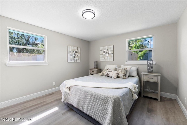 bedroom with multiple windows, baseboards, and wood finished floors