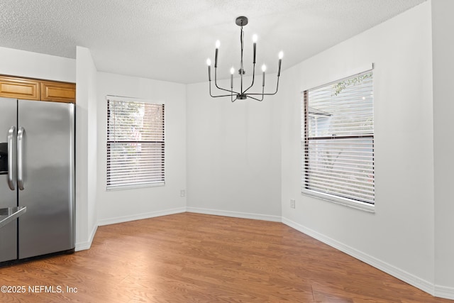 unfurnished dining area featuring a textured ceiling, light wood finished floors, a chandelier, and baseboards