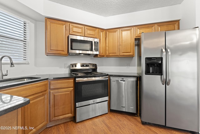 kitchen with dark countertops, light wood-style flooring, stainless steel appliances, a textured ceiling, and a sink