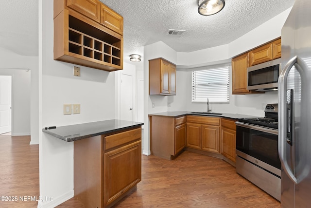 kitchen featuring visible vents, appliances with stainless steel finishes, brown cabinetry, a sink, and wood finished floors