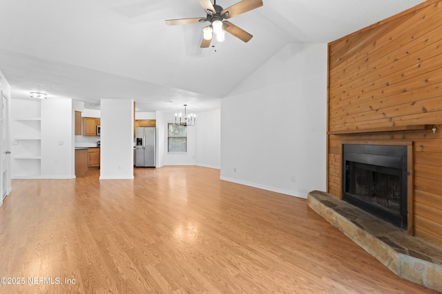 unfurnished living room featuring lofted ceiling, a fireplace, light wood finished floors, and ceiling fan with notable chandelier