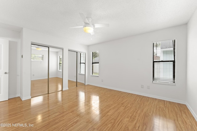 unfurnished bedroom featuring light wood-style floors, multiple windows, multiple closets, and a textured ceiling