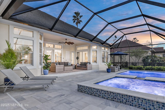 patio terrace at dusk featuring a lanai, outdoor lounge area, an outdoor pool, a ceiling fan, and an in ground hot tub