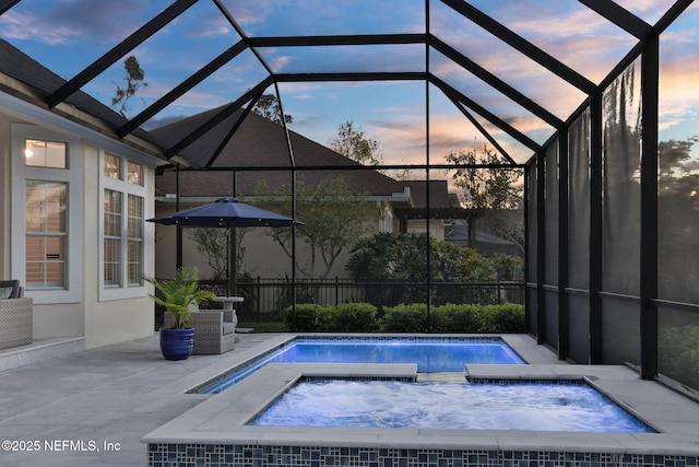 pool at dusk featuring glass enclosure, an in ground hot tub, and a patio area