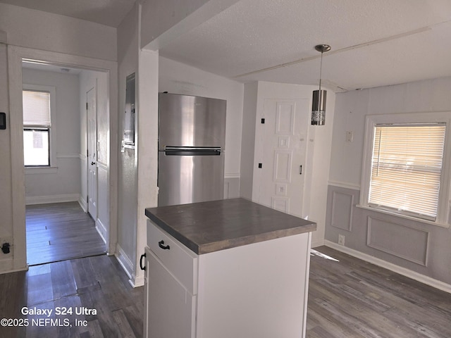 kitchen featuring dark wood-style floors, decorative light fixtures, dark countertops, freestanding refrigerator, and white cabinets