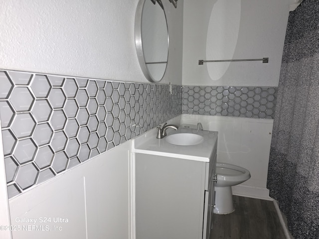 bathroom with toilet, a wainscoted wall, wood finished floors, vanity, and tile walls