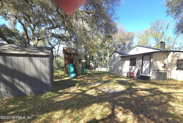 view of yard featuring entry steps, a playground, an outdoor structure, and a storage shed