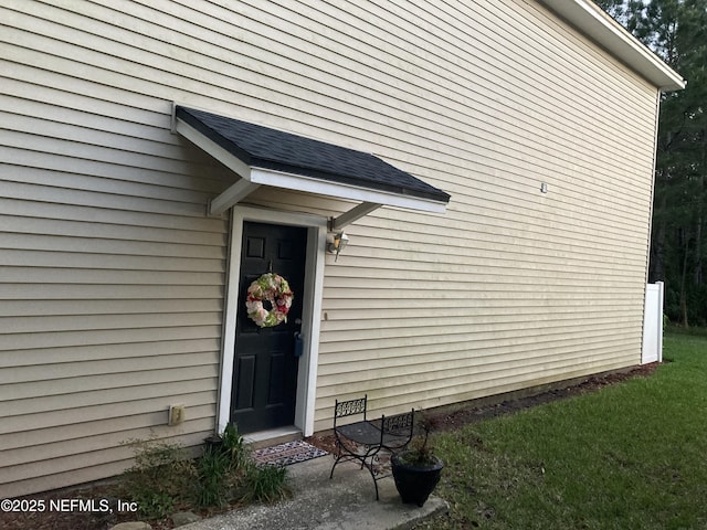 view of exterior entry featuring a yard and roof with shingles