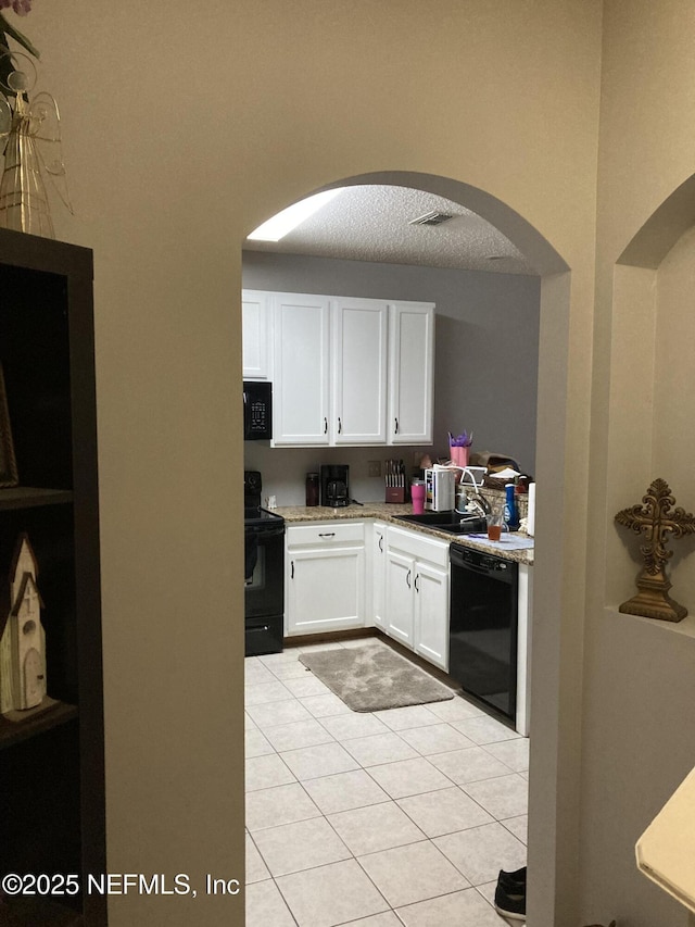 kitchen featuring black appliances, light stone countertops, light tile patterned flooring, white cabinetry, and a sink