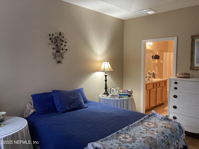 bedroom featuring visible vents, connected bathroom, a textured ceiling, and light wood-type flooring