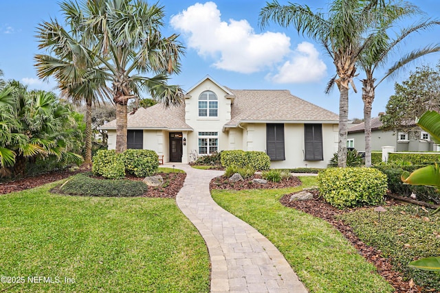 view of front of home with a front yard, roof with shingles, and stucco siding