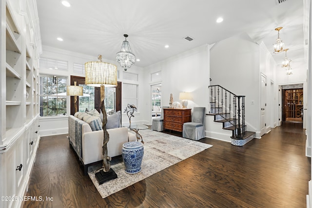 living area with plenty of natural light, dark wood-type flooring, an inviting chandelier, and stairs