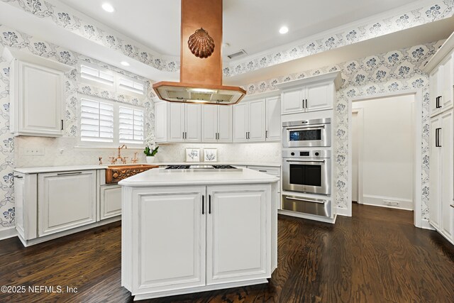 kitchen featuring cooktop, light countertops, island exhaust hood, stainless steel double oven, and a warming drawer