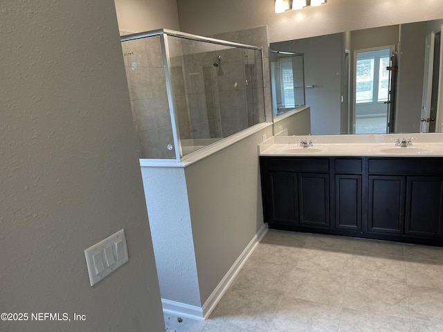 full bathroom with double vanity, tiled shower, baseboards, and a sink