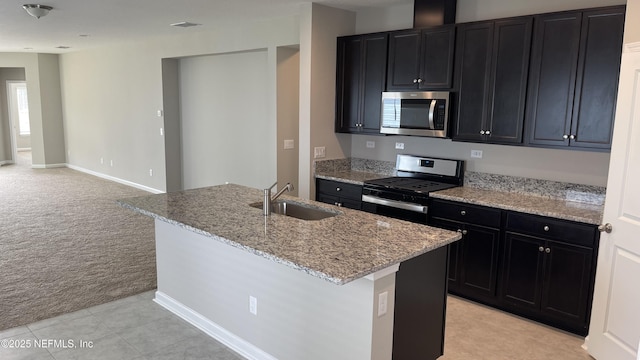 kitchen with light carpet, a sink, stainless steel appliances, light stone countertops, and dark cabinets