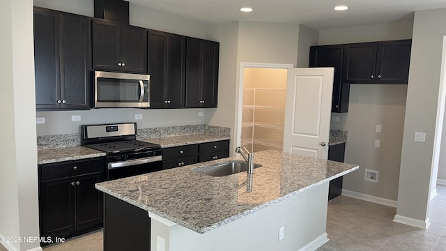 kitchen with a sink, light stone counters, stainless steel appliances, light tile patterned floors, and dark cabinets