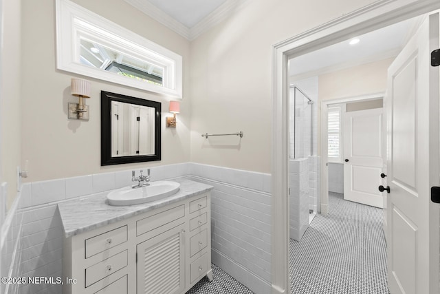 bathroom featuring tile walls, crown molding, a wainscoted wall, a stall shower, and vanity