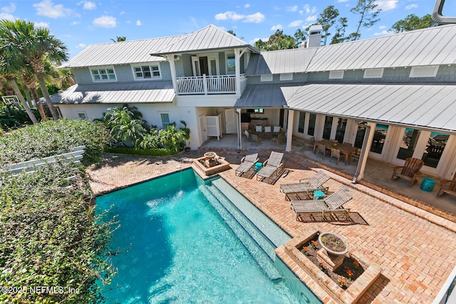 rear view of house with a balcony, an outdoor pool, a chimney, a patio area, and metal roof