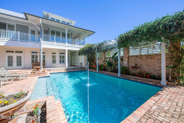 rear view of property with a patio, fence, french doors, a fenced in pool, and a balcony