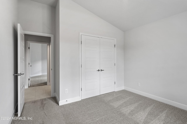 unfurnished bedroom with lofted ceiling, a closet, carpet flooring, and baseboards