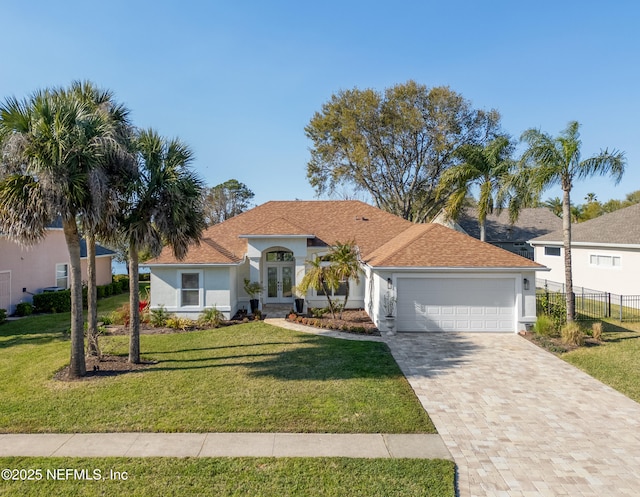 mediterranean / spanish home featuring stucco siding, decorative driveway, french doors, a front yard, and an attached garage