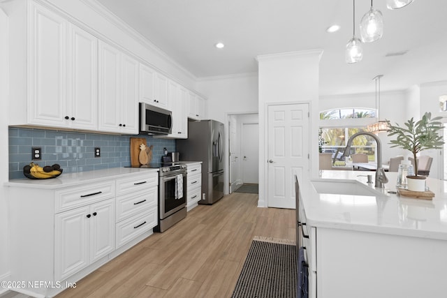 kitchen with a sink, stainless steel appliances, white cabinetry, crown molding, and tasteful backsplash