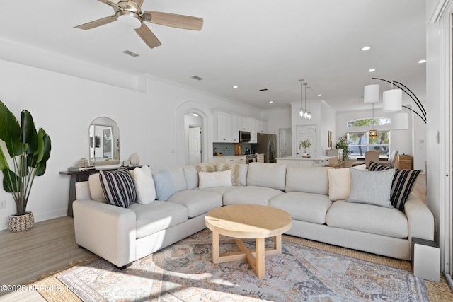 living room featuring visible vents, a ceiling fan, recessed lighting, arched walkways, and light wood-style floors