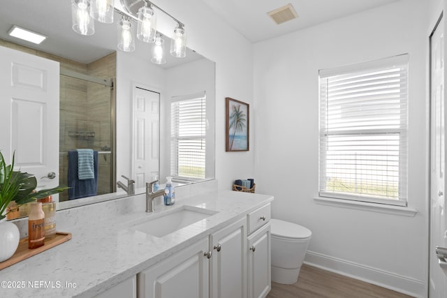 bathroom featuring visible vents, baseboards, tiled shower, wood finished floors, and vanity