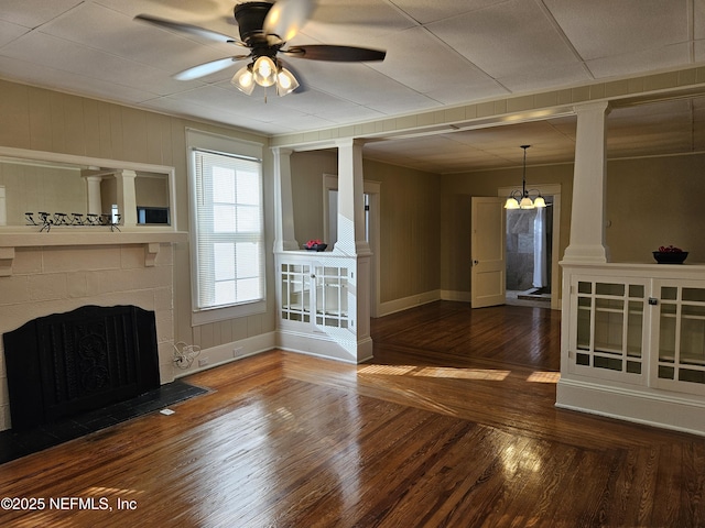 interior space featuring a tile fireplace, wood finished floors, a ceiling fan, baseboards, and decorative columns