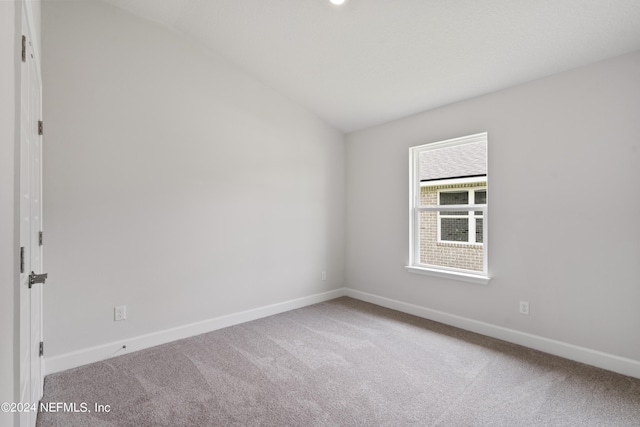 carpeted spare room with lofted ceiling and baseboards