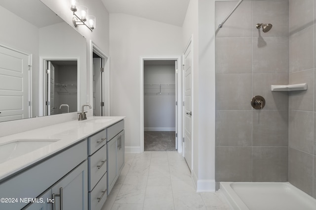 full bath with marble finish floor, a sink, a tile shower, and double vanity