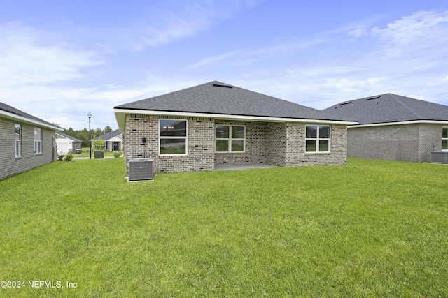 back of property featuring a shingled roof, brick siding, a yard, and central AC