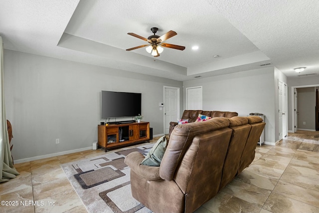 living room featuring visible vents, a ceiling fan, a tray ceiling, a textured ceiling, and baseboards