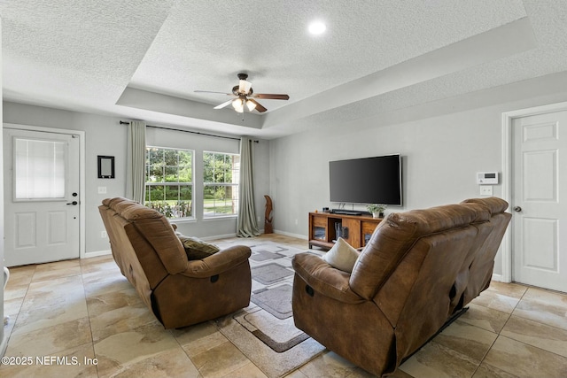 living room with a tray ceiling, a ceiling fan, baseboards, and a textured ceiling