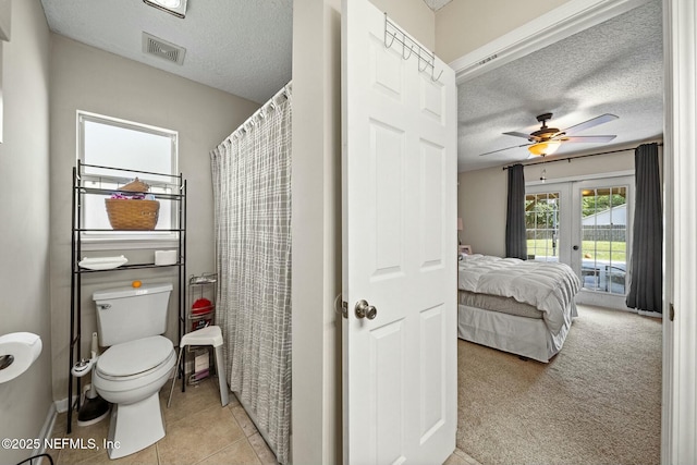 ensuite bathroom featuring french doors, toilet, tile patterned flooring, and a textured ceiling