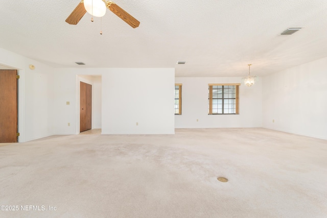 spare room featuring ceiling fan with notable chandelier, light colored carpet, visible vents, and a textured ceiling