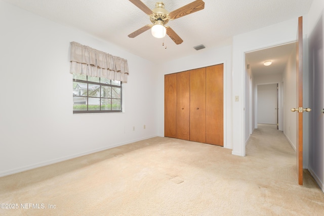 unfurnished bedroom featuring baseboards, visible vents, a closet, a textured ceiling, and light carpet