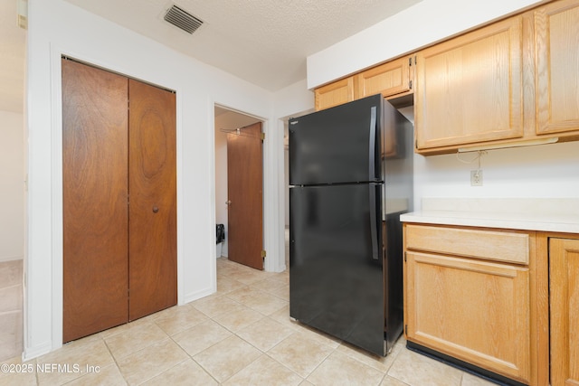 kitchen with light tile patterned floors, a textured ceiling, light countertops, and freestanding refrigerator